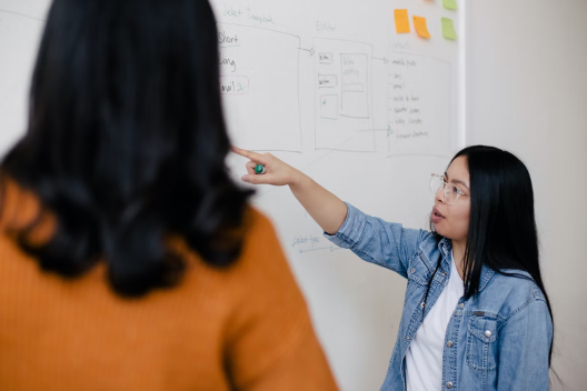 Women explaining something on a whiteboard to a coworker.